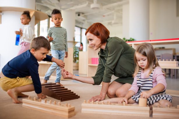 Nursery school children with teacher sitting on floor indoors in classroom, montessori learning.